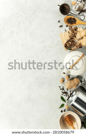 Flat lay of a white teapot, ginger, honey, loose leaf tea, and accessories on a stone surface with generous space for text 