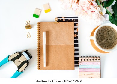 Flat lay of white working table background with cup of coffee. Top view scrapbooking tools, peonies, golden paper binder clips, blank greeting card, craft Notebook and pen. Desktop mock up planner.