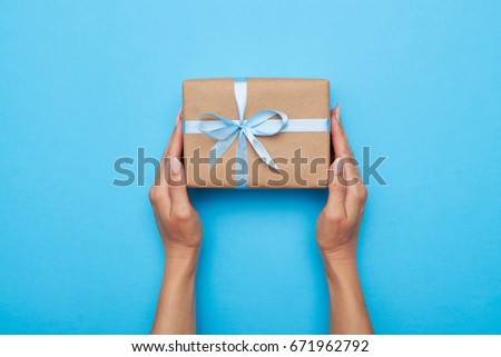Flat lay of woman hands holding gift wrapped and decorated with bow on blue background with copy space