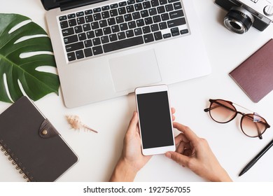 Flat Lay Of Woman Hands Using Mobile Phone With Travel Item And Laptop On Desk. Summer, Holiday, Work And Planning Travel Concepts. Top View And Copy Space