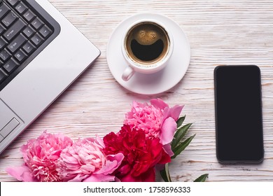 Flat lay women's office desk. Female workspace with laptop, pink peonies bouquet and coffee on white background. Top view feminine background.