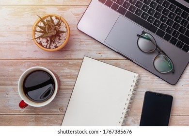 Flat lay of working space on wooden desktop background, laptop, blank spiral notebook, succulent and coffee. Top view