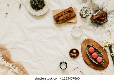 Flat lay of workspace with copy space, notebook, plants, pastel pink macaroons, woman accessories on white bedsheets background. Flat lay, top view blogger influencer home office concept.