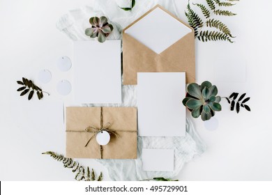 Flat lay workspace. Wedding invitation cards, craft envelopes, pink and red roses and green leaves on white background. Overhead view, top view - Powered by Shutterstock