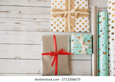 Flat lay of wrapped gift boxes and shiny wrapping paper rolls on white wooden surface. Perfect for holiday prep, DIY gift ideas, and seasonal content