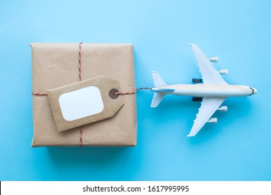 Flat Lay Of Wrapped Package With Blank Tag And Airplane Model On Pastel Blue Background. Shipping Logistics Transport Minimal Creative Concept.