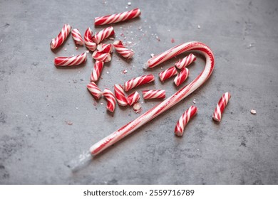 flat lay of a wrapped up red and white Christmas candy cane and broken pieces of a candy cane against a gray background - Powered by Shutterstock