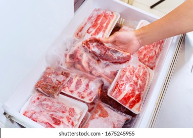 Flat layout of human hand picking a package of red meat, plastic wrapped from the freezer box in the storage room