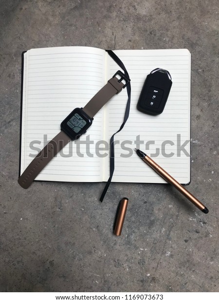 Flat layout of personal belongings, notes\
book, pen, watches, car key and\
money.