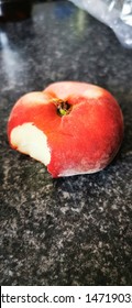 Flat peach fruit with a big bite taken out of it shot at a 45 degree angle on the kitchen grannit worktop