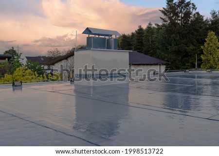 Flat roof covered with bitumen membrane and silver lacquer with chimney on a private house. Reflections after rain
