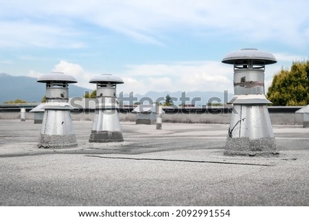 Flat roof vents on building with 2-ply SBS or modified bitumen roofing system. Group of metal ventilators such as: bathrooms and laundry exhaust and plumbing stack vent. Selective focus.