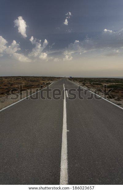 Flat straight deserted road, that crosses some\
deserted fields, located in the south part of Karpathos island\
Greece, during afternoon\
hours.