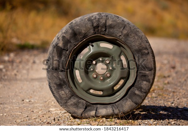 A flat tire and a bent car rim sit on\
the side of the road. Severely damaged car wheel after a car\
accident. Kazakhstan, Shymkent September 20,\
2020
