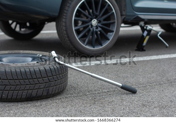 A flat tire car wheel and screwdriver are on a\
asphalt road on the broken Skoda Rapid background. Jack is lifting\
up a vehicle. Automobile service. Tire replacement concept, Prague,\
March, 2020.
