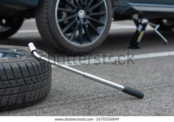 A flat tire car wheel and screwdriver are on a\
asphalt road on the broken Skoda Rapid background. Jack is lifting\
up a vehicle. Automobile service. Tire replacement concept, Prague,\
March, 2020.