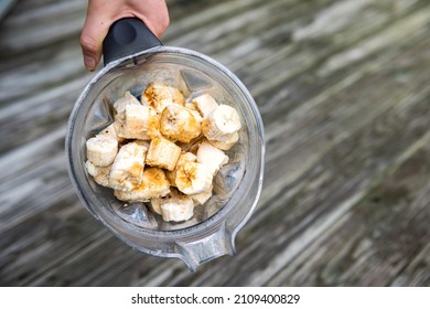 Flat Top Closeup Of Hand Holding Frozen Peeled Yellow Bananas In Plastic Blender Container For Fruit Homemade Smoothie Or Vegan Non-dairy Nice Ice Cream