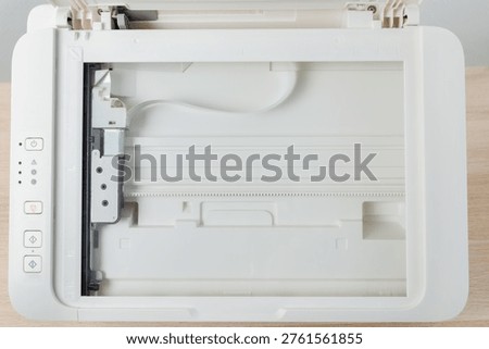 Flatbed scanner bed inside a multifunction office printer shown from above. Clean empty glass surface, control buttons and mechanism visible, document scanning, office tech and productivity.