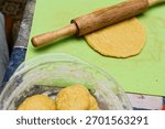 Flatbread dough gets rolled out on green silicone mat using wooden rolling pin in cozy kitchen. Flour dusted dough balls sit in glass bowl, adding rustic charm to homemade bread-making scene.