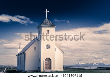 Flateyjarkirkja white lutheran church with meadow in foreground and sea  fjord with dark blue sky and mountains in the background, Flatey, Iceland