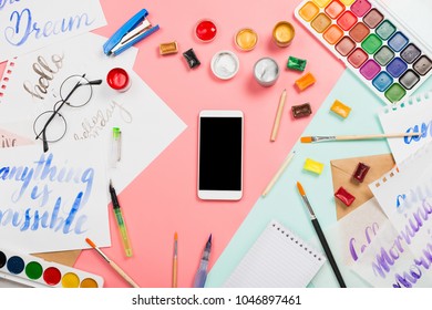 Flatlay arrangement with watercolors, brushes, glasses, brushpen, paints with smartphone with black copyspace and other stationary and art supplies. Creativity, education, lettering practice concept - Powered by Shutterstock