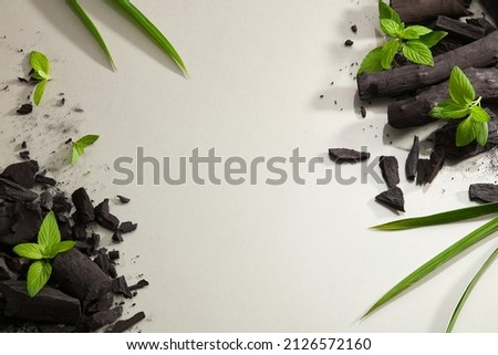 Flatlay of bamboo activated charcoal and charcoal powder decorate with green leaf in white background 