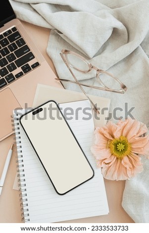 Flatlay blank mobile phone screen with copy space, glasses, laptop computer, earphones, stationery, crumpled cloth on peachy table. Office desk workspace. Business, work template. Flat lay, top view