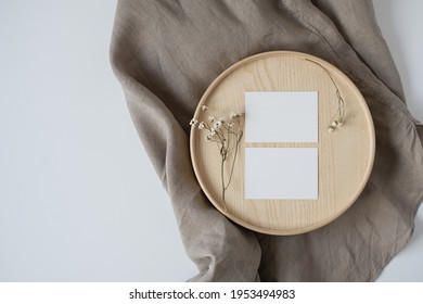 Flatlay of blank paper business cards with mockup copy space and flowers on wooden tray on neutral beige blanket background. Aesthetic minimal business template for social media. Flat lay, top view