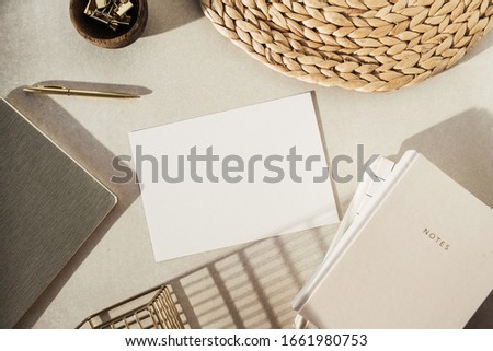 Flatlay blank paper sheet, notebooks, clips in wooden bowl, straw stand on beige concrete background. Home office desk workspace. Business, work template. Flat lay, top view.