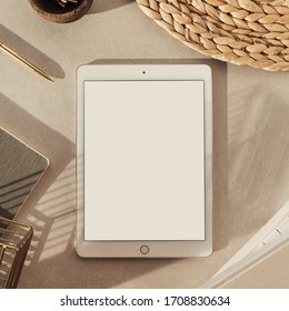 Flatlay of blank screen tablet, notebooks, clips in wooden bowl, straw stand on beige concrete background. Home office desk workspace. Business, work template. Flat lay, top view.
