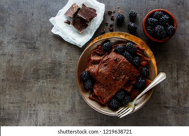 Flat-lay of chocolate crepes. Thin pancakes, chocolate bars and fresh blackberries