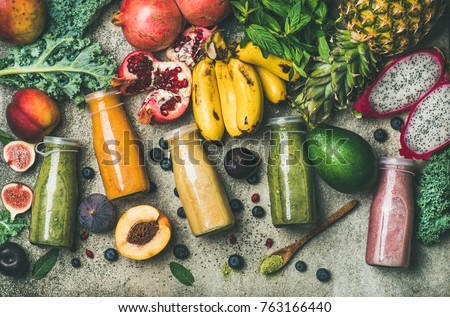 Flat-lay of colorful smoothies in bottles with fresh tropical fruit and superfoods on concrete background, top view. Healthy, clean eating, vegan, vegetarian, detox, dieting breakfast food concept