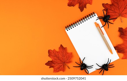 Flatlay composition with blank notepad, pen, autumn leaves and spiders on orange background. Happy Halloween. Top view. Copy space. - Powered by Shutterstock