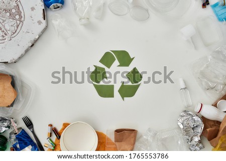 Flatlay composition with different waste, garbage types and recycling sign made of paper in the center over white background. Sorting, recycling waste concept. Horizontal shot. Top view