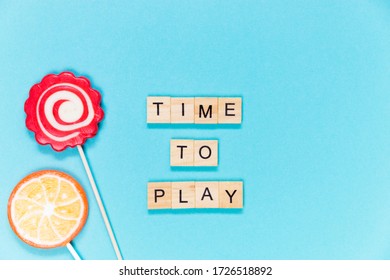 Flatlay concept time to play, sween lollipops and letters wooden cube on blue background. Selective focus.