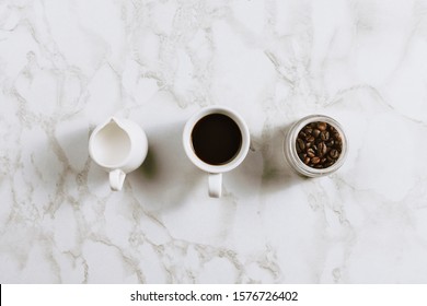 Flatlay Of Creamer With Plant-based Milk, Cup Of Coffee And Jar With Beans On Marble