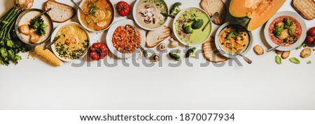 Flat-lay of creamy homemade soup in plates with bread slices over white plain table background, top view, copy space. Autumn Winter creamy vegan soups, vegetarian food menu, comfort food concept