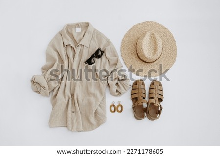 Flatlay of elegant stylish women's beach clothes and accessories. Aesthetic luxury summer fashion composition. Muslin t-shirt, straw hat, leather sandals, sunglasses, earrings. Flat lay, top view