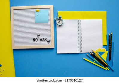 Flatlay Empty Letter Board With The Words No War, Patriotic Colors Of Ukraine Badge Heart, Blue Yellow Black Pencils, Blue Alarm Clock And Sticker, Notepad With Blank White Pages