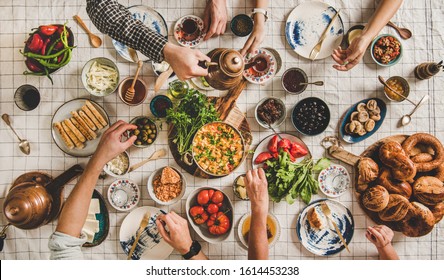 Flat-lay Of Family Having Turkish Breakfast With Pastries, Vegetables, Greens, Spreads, Cheeses, Fried Eggs, Jams And Tea In Tulip Glasses And Copper Teapots Over Pastel Chekered Linen Tablecloth