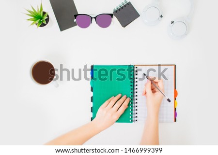 Flatlay with female hands making notes in a notepad. Home office workspace. White minimalistic background.