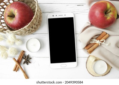 Flatlay Frame Arrangement With White Smartphone With Black Copyspace, Red Apples, White Candle, Cinnamon And Other Fall Decorations On White Wood Background. Autumn Composition.