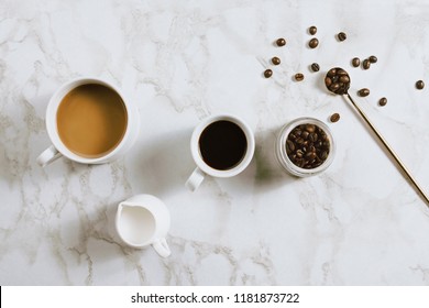 Flatlay Of Fresh Cups Of Espresso And Milk Coffee, Creamer, Coffee Beans And Spoon On Marble Background, Selective Focus