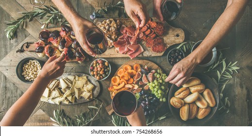 Flat-lay of friends eating and drinking together. Top view of people having party, gathering, celebrating at wooden rustic table set with various wine snacks and fingerfoods. Hands holding glasses - Powered by Shutterstock