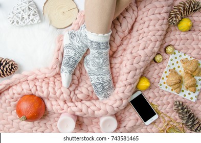 Flatlay Girl Legs In A Warm Socks On Background Of Merino Wool Handmade Knitted Large Blanket, Trendy Concept. Close-up Autumn And Winter Mood Flatly