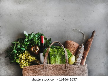 Flat-lay of healthy grocery shopping eco-friendly bag with vegetables, fruit, greens, bread, sausage, wine bottle over concrete background, top view, copy space. Local farmers market, shopping mall - Powered by Shutterstock