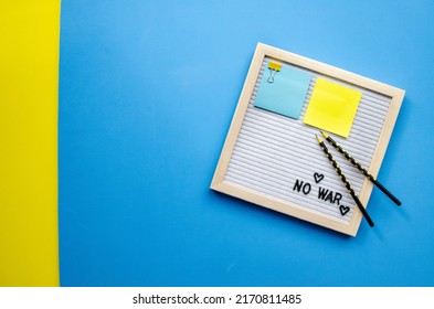 Flatlay Horizontal Composition Empty Letter Board With The Words No War, Pray For Ukraine, Patriotic Colors Blue And Yellow Sticker, Black Pencils, Empty Blue Background