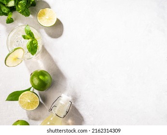 Flat-lay of mojito cocktail with lime, fresh mint and ice, bottle with mojito on white texture background close up. Summer refreshment citrus drink. Top view and copy space.