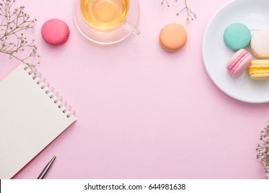 Flatlay Of Notebook, Cake Macaron, Cup Of Tea And Flower On Pink Table. Beautiful Breakfast With Macaroon.