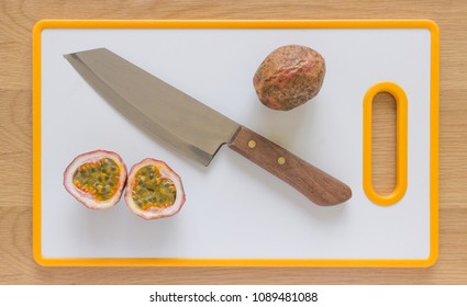 Flatlay Of One Cut And One Whole Passionfruit On A White Cutting Board With A Knife